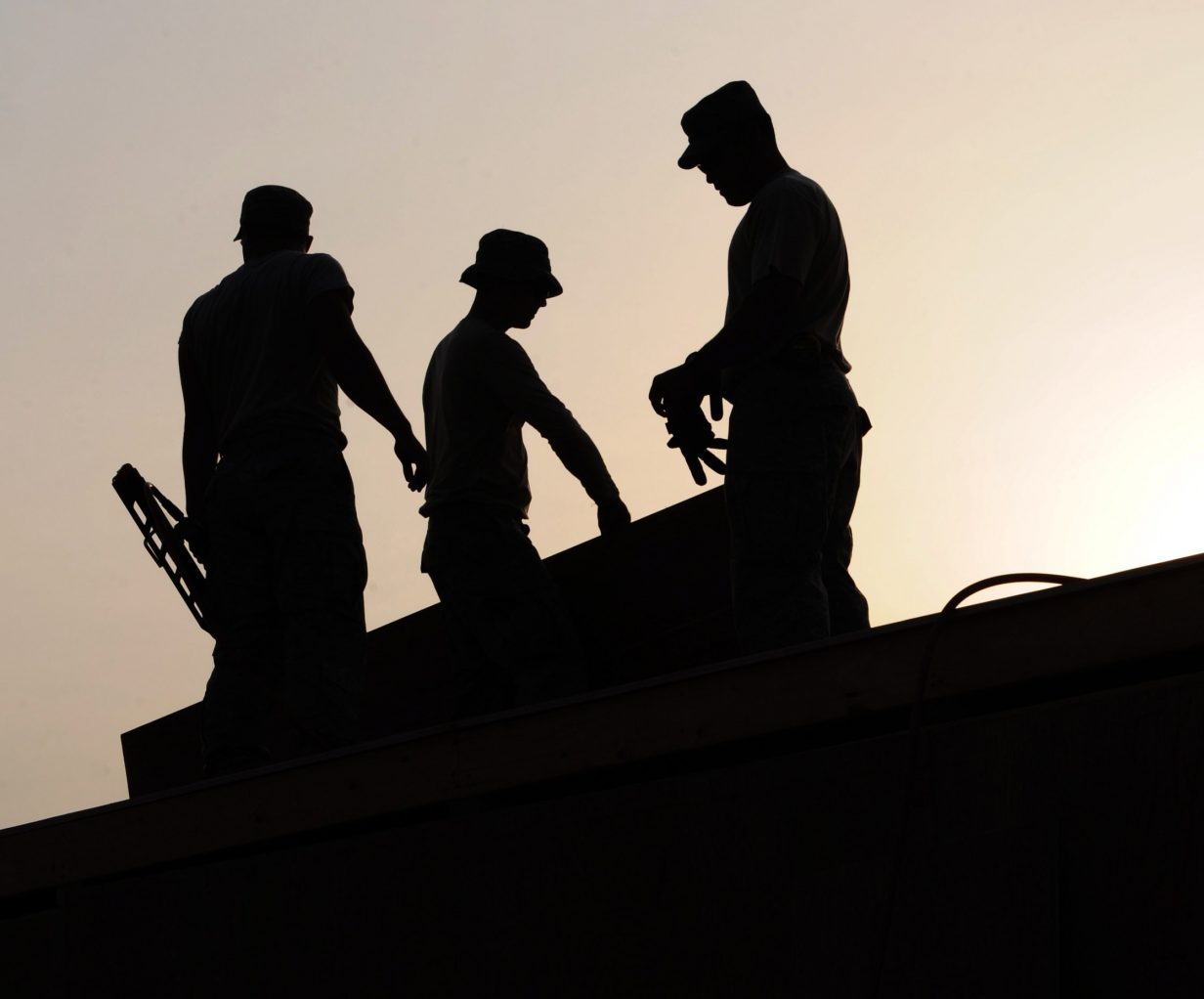 three person roof crew silhouettes on roof with sunset in back